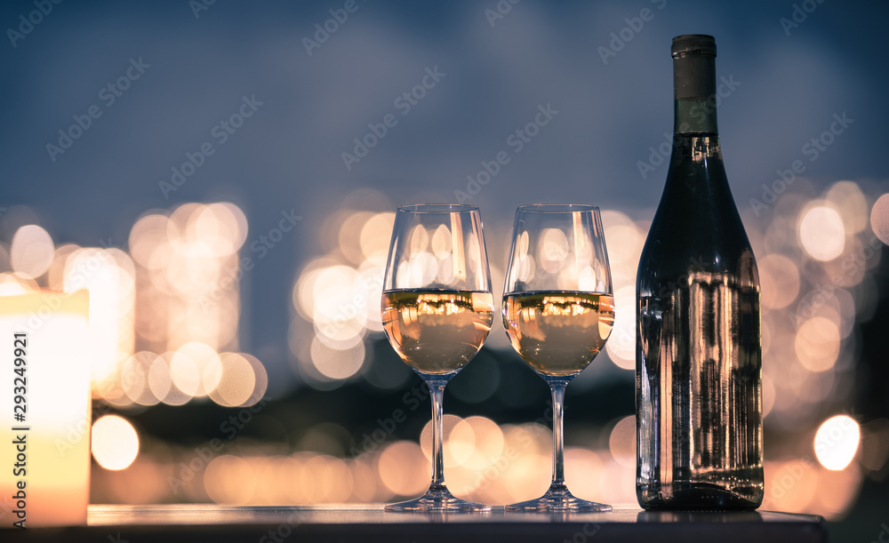 Pair of wine glasses in candle light dinner setting with city view in the background. 