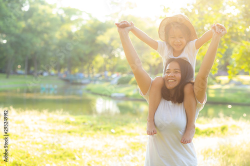 Beautiful young asian mother carrying little daughter with smile, child ride the neck on mom with happiness and cheerful together in the park, lifestyle family with enjoy and fun concept.