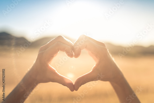 Hand shaped heart outdoors with natural sun flair.  Love and nature concept. 