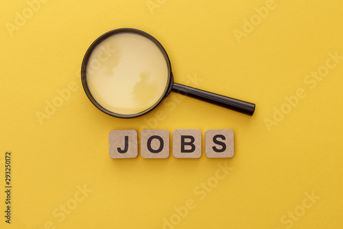 top view of magnifying glass near cardboard squares with jobs lettering on yellow background photo