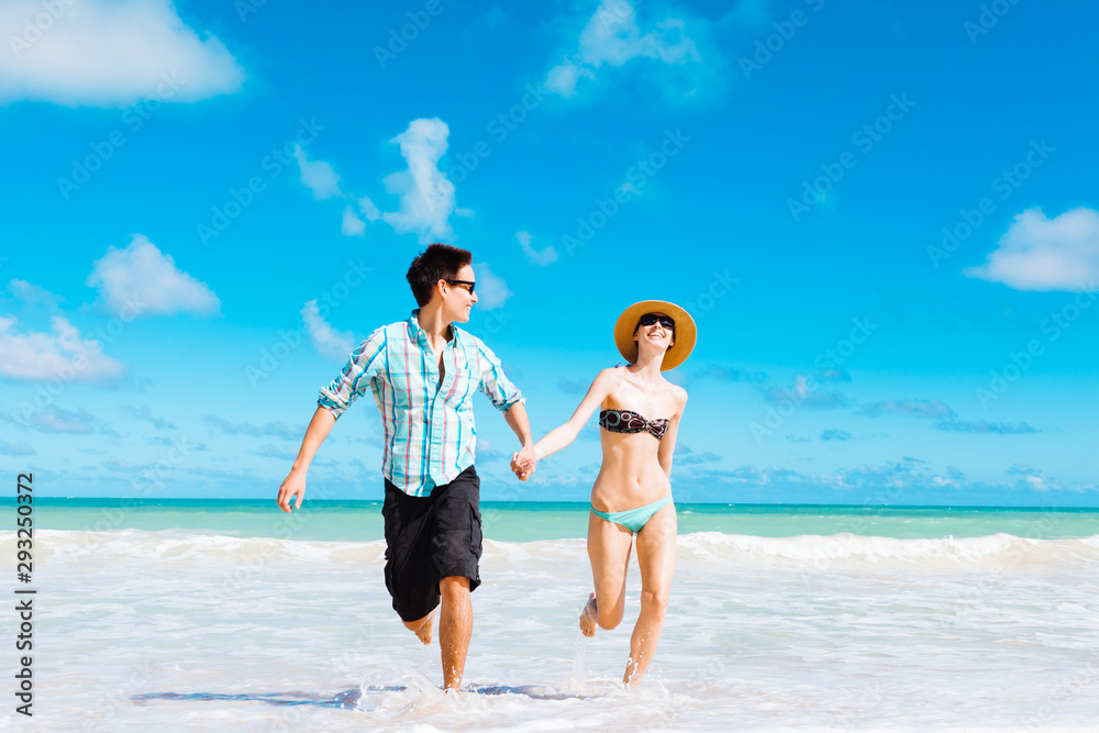 Happy couple on the beach running holding hands.