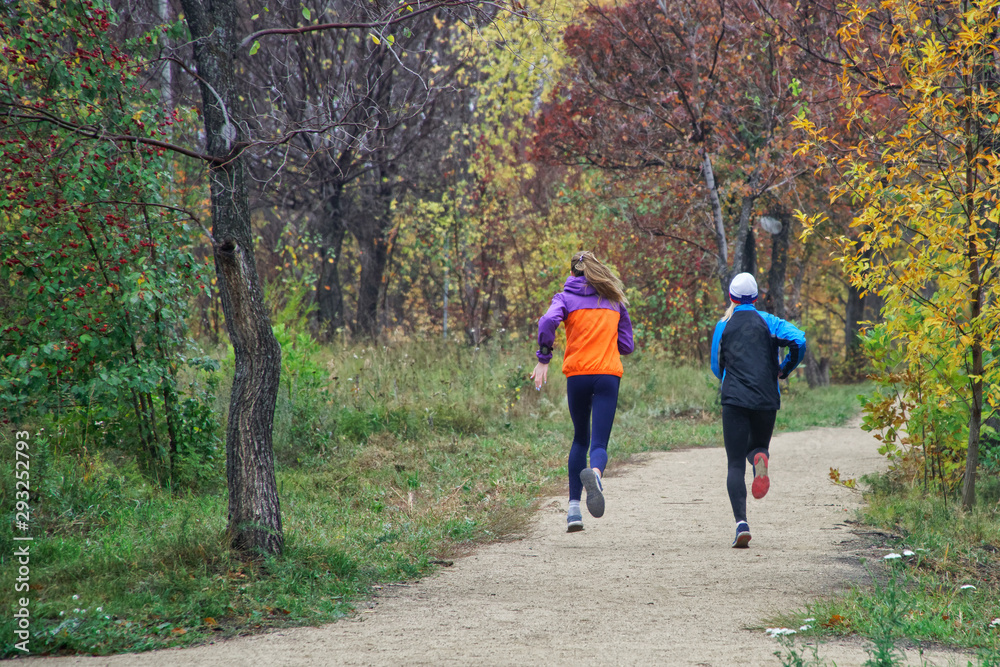 Young girls are training on the run in the autumn park alley. Activity and sport. Unrecognizable
