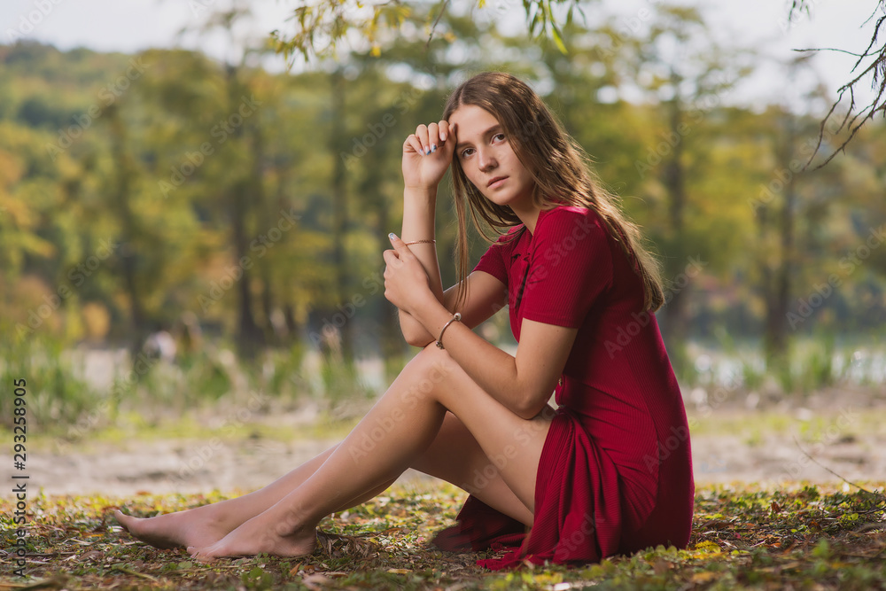 beautiful, young brown-haired woman in a red dress on the background of the morning lake with cypresses and sun rays in the fog beautiful, young brown-haired woman in a red dress on the background of the morning lake with cypresses and sun rays in the fog