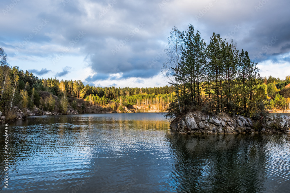 Autumn landscape. Stone island with trees in the middle of a lake surrounded by forest. Autumn landscape. Stone island with trees in the middle of a lake surrounded by forest.