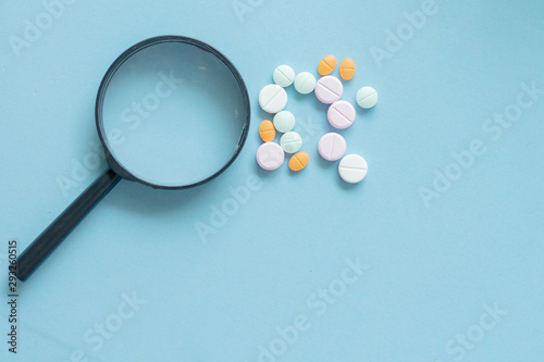 Magnifying glass with pills on blue background. pharmaceutical inspection identifies pills. Medicinal substance quality concept.