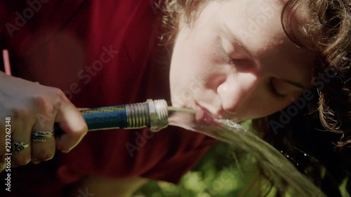 Closeup: Young woman sips water from a garden hose on a summer day