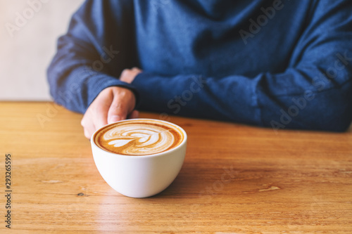 Closeup image of a hand holding a cup of hot coffee on wooden table