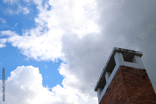 Closeup of brown brick chimney with dark white cloudy blue sky.