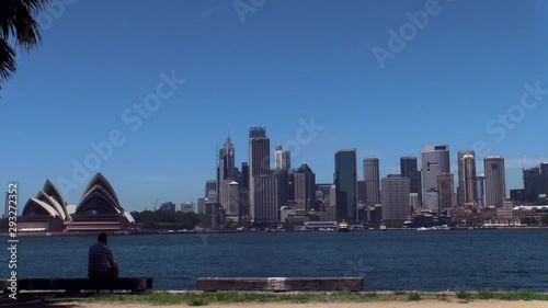 Man is one phone, sitting in shade with view on Sydney skyline and opera house photo