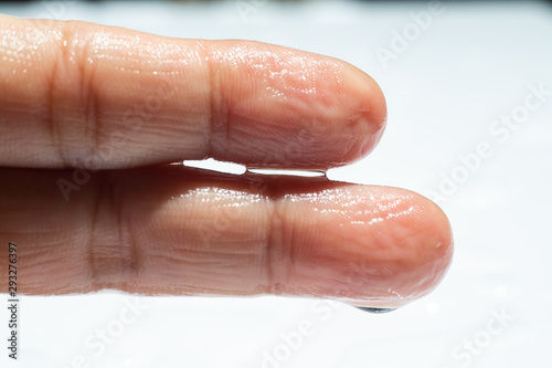 Woman's wet left hand with water drops on middle finger, White acrylic background, Close up & Macro shot, Selective focus, Asian Body skin part, Relaxing Bath, Healthcare concept