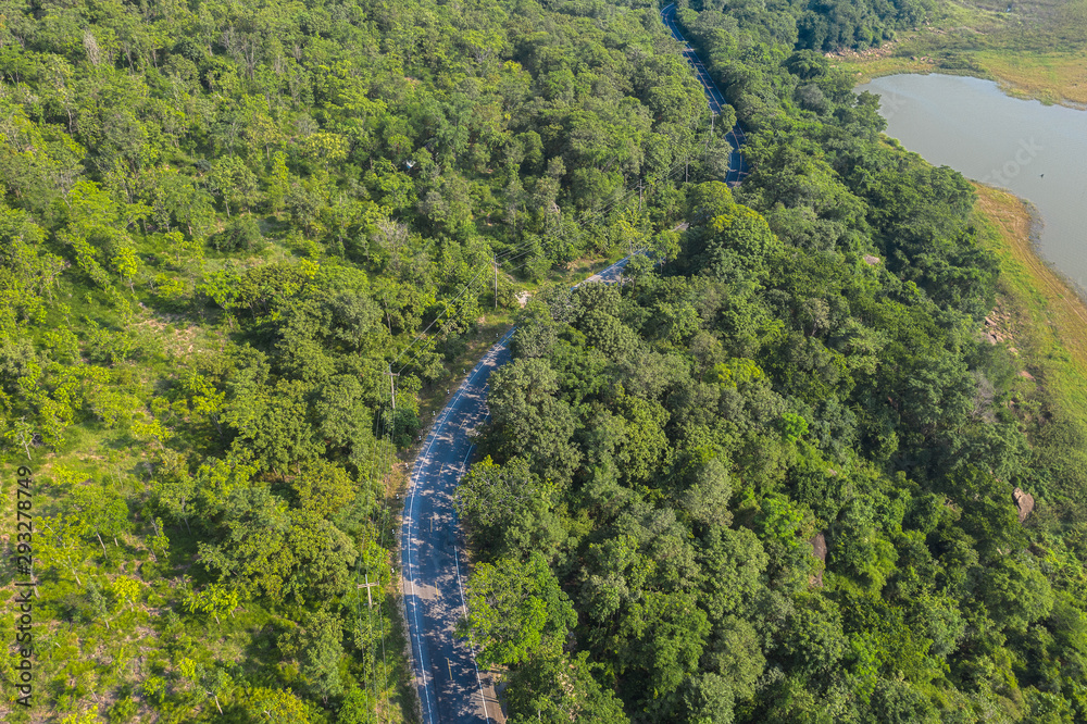 Aerial top view over mountain rural road in tropical rainforest with green tree, road going through forest from above by drone.