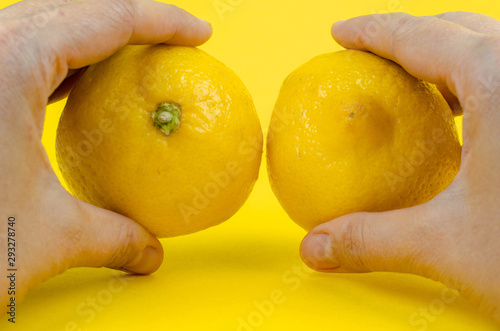 Two half of lemon in hands on yellow background