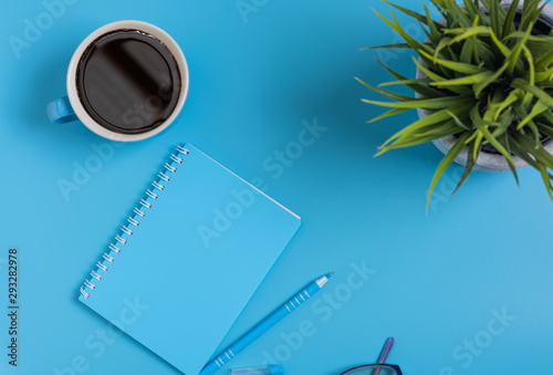 Work space blue set of note pad,pen,eyeglasses and coffee cup on blue desk background,top view