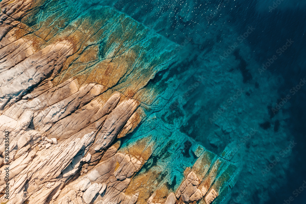 Aerial view of a slide turn from a drone on the view of calm turquoise sea water and rocks from molten lava. Pattern of sea surface and rocky shore. Thracian Sea, Greece. Rocky coast of the peninsula