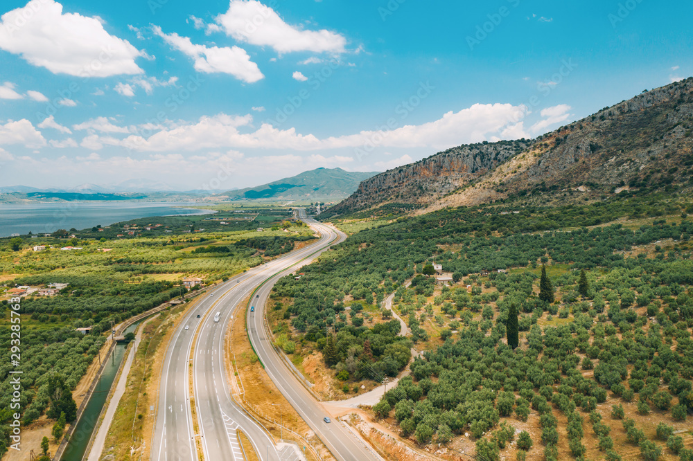 Aerial view of a drone plantation with olive trees, planted in straight rows against the background of the blue sea, sky and mountain peaks. Olive garden. Olive tree - a symbol of Greece gardenˈ