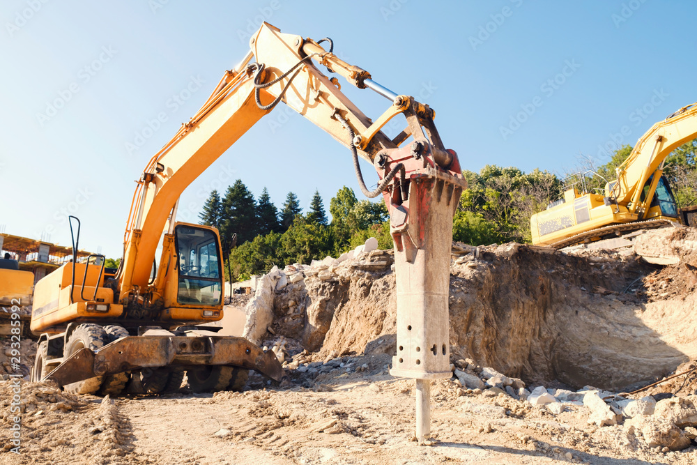 A large yellow construction equipment is digging a pit for the base of a residential complex with an industrial jackhammer. Construction of a large residential building. Initial construction phase A large yellow construction equipment is digging a pit for the base of a residential complex with an industrial jackhammer. Construction of a large residential building. Initial construction phase