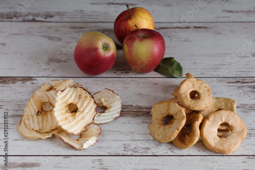 Dried apple rings and apple crisp chips in comparison with fresh red apples.