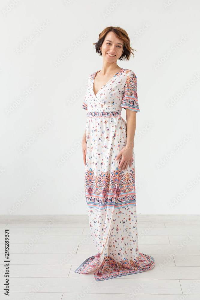 Charming young woman posing on a white background in a long light bright summer dress. The concept of exquisite women's clothing. Charming young woman posing on a white background in a long light bright summer dress. The concept of exquisite women's clothing.