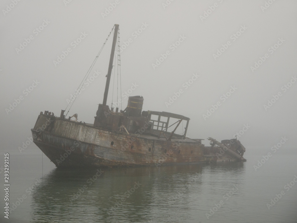 An old wooden shipwreck whaling boat abandoned stand on beach on foggy morning 
