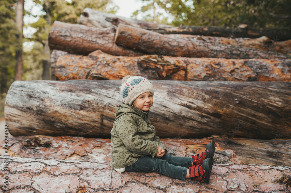 Autumn portrait of little girl in the autumn park on stack of logs. Side view. Autumn portrait of little girl in the autumn park on stack of logs. Side view.