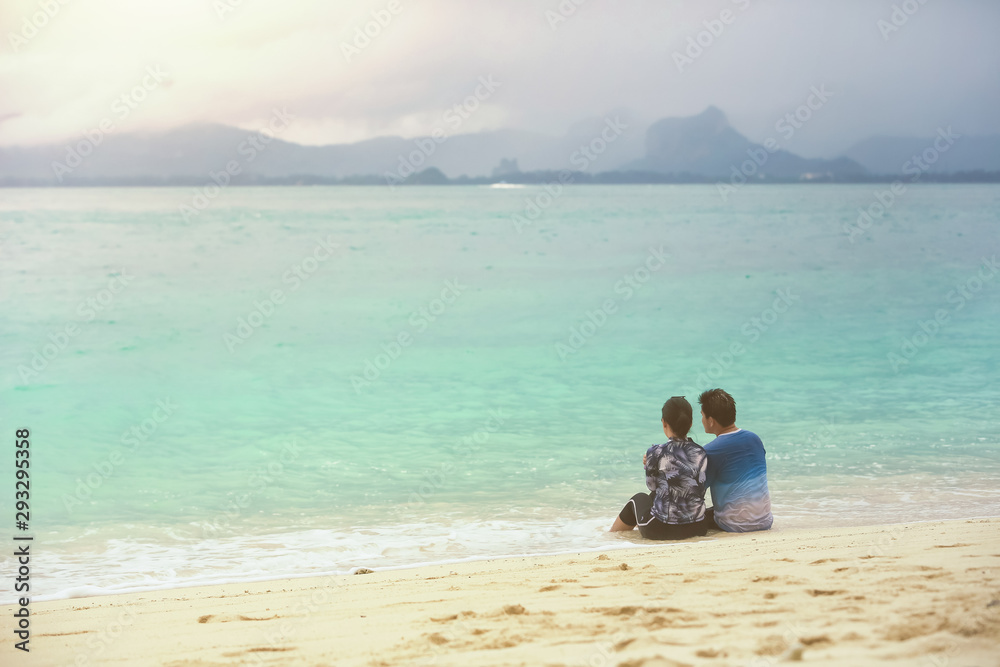 Lovers couple are sitting on the shore of a tropical beach in the evening.