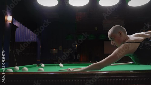 stylish bald girl in a black leather corset plays billiards.
