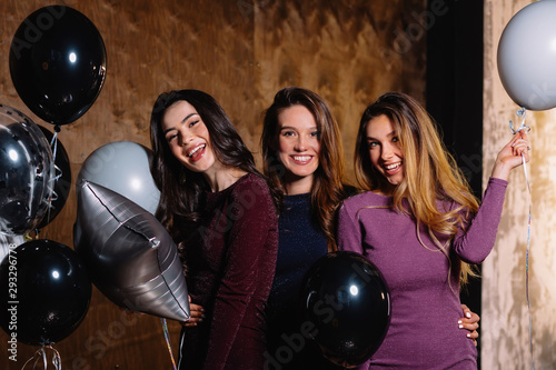 Studio shot of three attractive young women wearing evening holiday dresses preparing for party with balloons