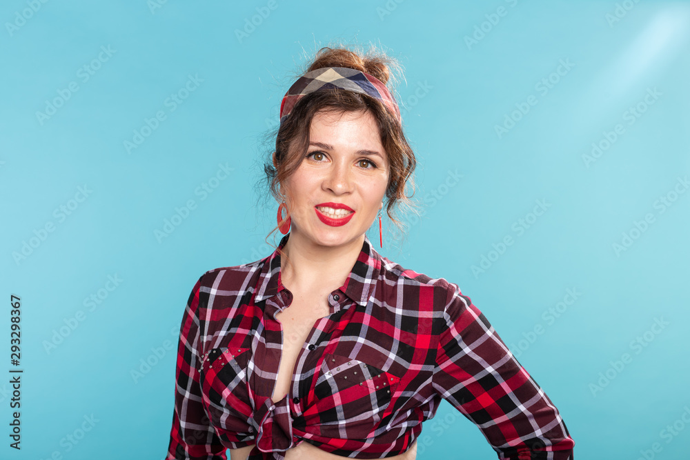 Fototapeta premium Positive beautiful young woman in a plaid vintage shirt looking at the camera and smiling posing on a blue background.