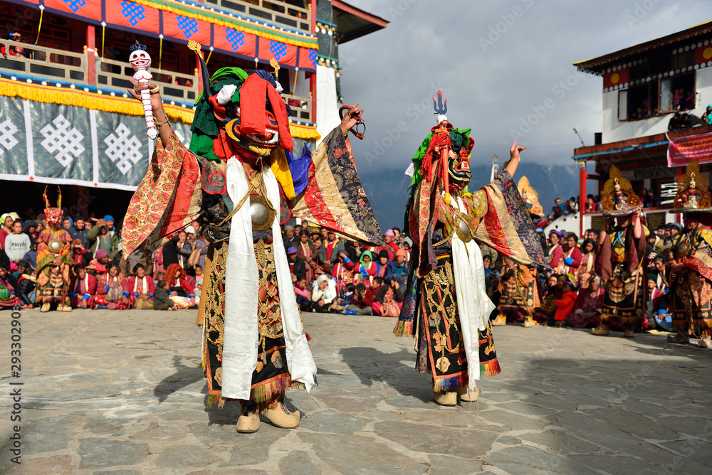 Tawang, Arunachal Pradesh, India, Buddhist monk dancing in disguise for the Torgya  festival, in the background there are monastery and many gathered viewers.