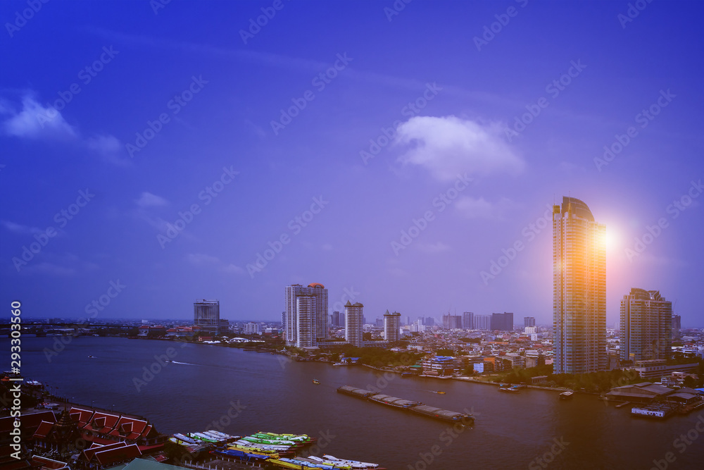 Naklejka premium Wide scene drone picture of high angle view group of home and Chaopraya river in Bangkok the capital city of Thailand with sand container tugboat and colorful morning sunrise background.