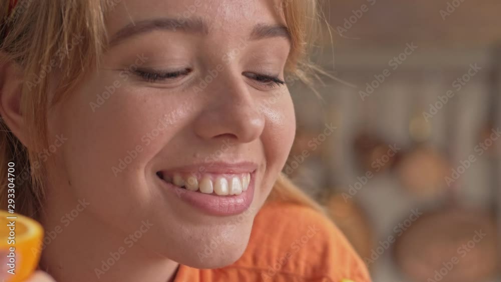 Cropped view of cheerful young woman holding two half of orange and sniffing it while cooking at the kitchen