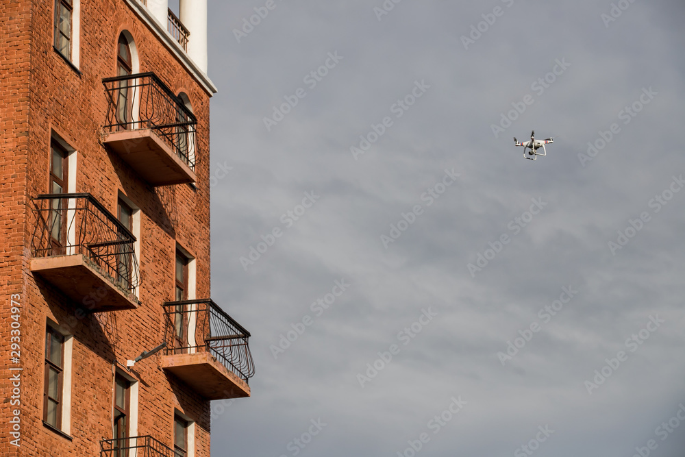 Quadrocopter unmanned camera hovers in bright blue sky above city on background of urban buildings Modern technology photo and video shooting bird