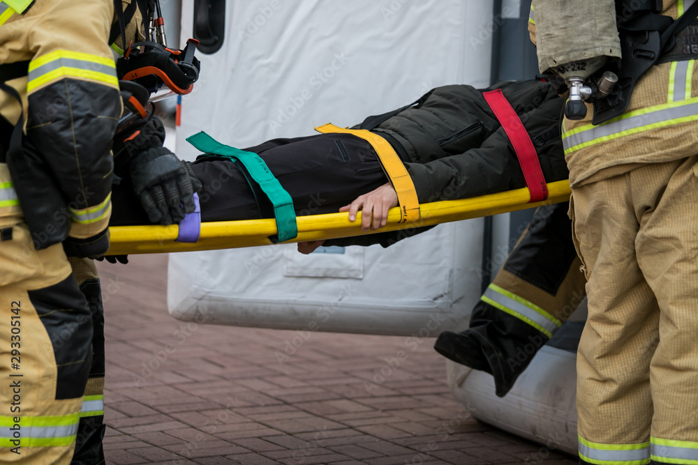  professional firefighter firefighters fireproof suits, white helmets and gas masks carry the injured person on stretchers