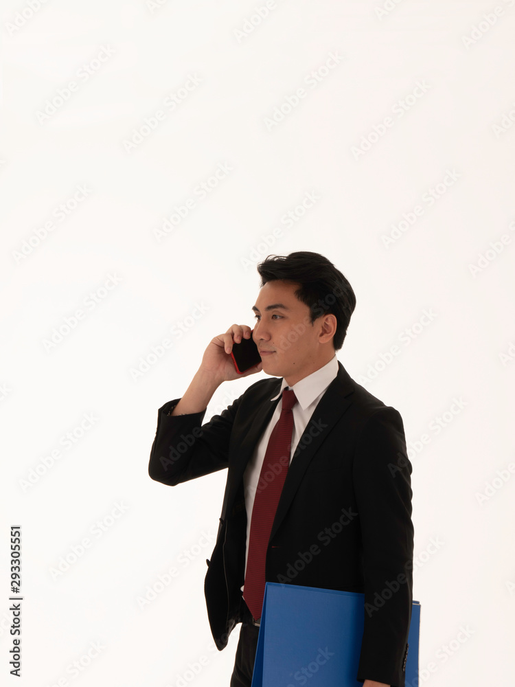 An attractive young Asian businessman talking on the phone, holding paperwork file with a white background. An attractive young Asian businessman talking on the phone, holding paperwork file with a white background.