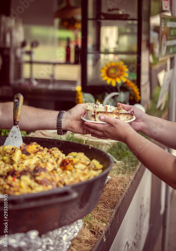 Seller at a food stand serves a serving of traditional Slovenian food. The food is fried in a large skillet. Vertical image with warm colors