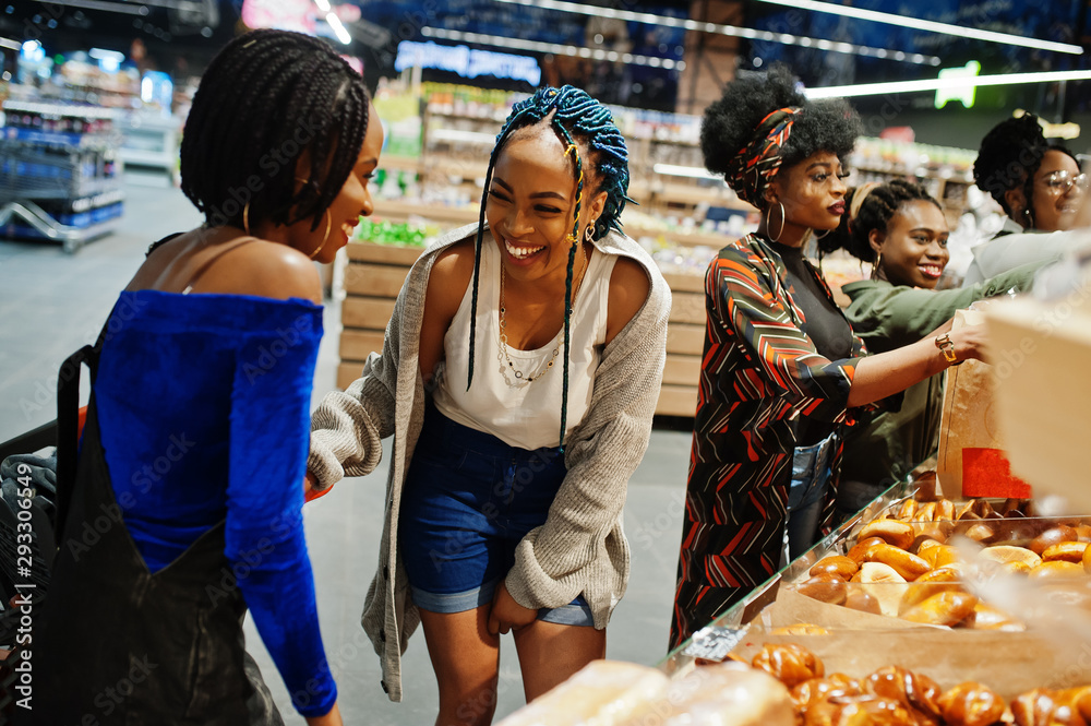 Group of african womans with shopping carts near baked products at a supermarket.