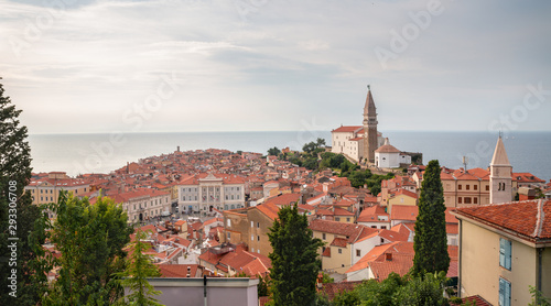Piran is beautiful old city located in south Slovenia. A view of St George's Church and the red tiled rooftops of the old town. In the background you can see the Adriatic Sea