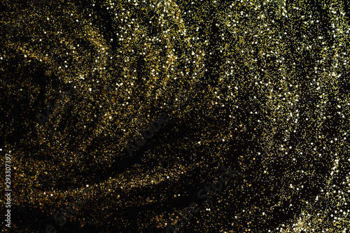 Golden glitter scattered on the black card background, top view. Abstract pattern created by hand, imitaion of storm, selective focus photo