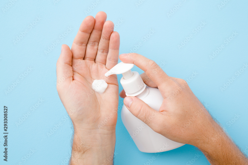 Perfect groomed man hands holding white bottle and using moisturizing cream on pastel blue background. Care about clean, soft and smooth body skin. Closeup. Perfect groomed man hands holding white bottle and using moisturizing cream on pastel blue background. Care about clean, soft and smooth body skin. Closeup.