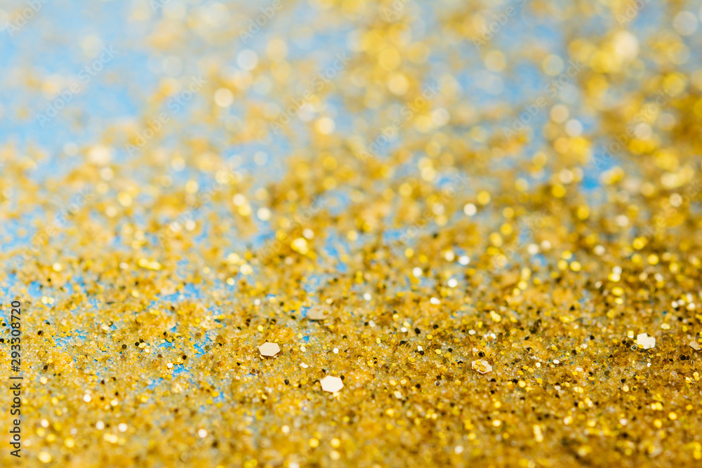Masses of golden glitter scattered on the blue card background, top view, shallow depth of field selective focus Masses of golden glitter scattered on the blue card background, top view, shallow depth of field selective focus