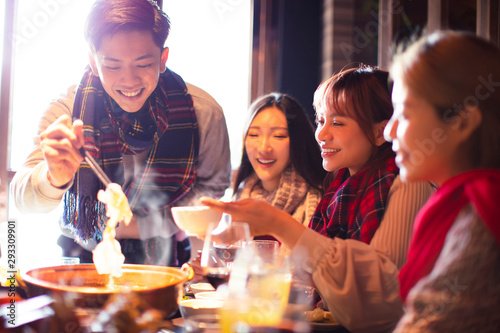 happy young friends eating hot pot in restaurant at winter