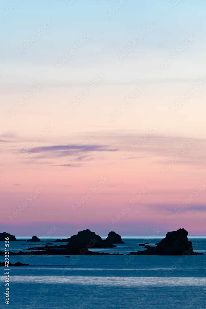 sunset at the beach with a calm ocean and rocks and reefs under a lilac purple sky