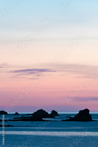 sunset at the beach with a calm ocean and rocks and reefs under a lilac purple sky