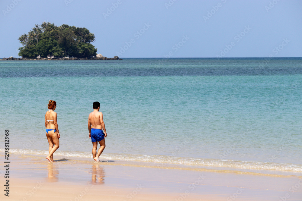 Young couple on the tropical beach go swimming to the azure sea. Woman in blue bikini and man walking on background of paradise island with coconut palm trees, romantic vacations concept Young couple on the tropical beach go swimming to the azure sea. Woman in blue bikini and man walking on background of paradise island with coconut palm trees, romantic vacations concept