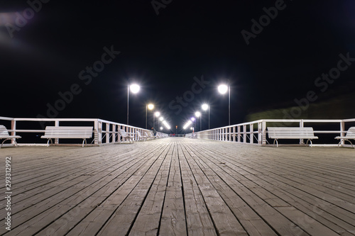 Wooden pier by the sea lit by lamps at night.