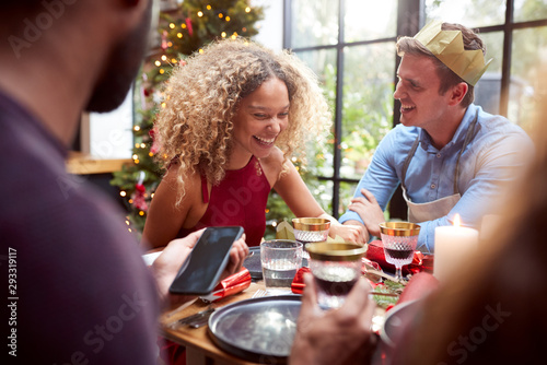 Couple Sitting Around Dining Table At Home For Christmas Dinner With Friends Talking