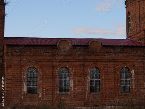 Old brick wall with towers, arched windows and iron bars background of blue sky. Ancient building closeup.