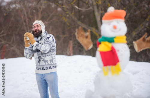 Snowman and cheerful bearded hipster knitted hat and warm gloves play with snow outdoors. Christmas holidays. Active lifestyle. Snow games. Leisure on fresh air. Have fun winter day. Let it snow