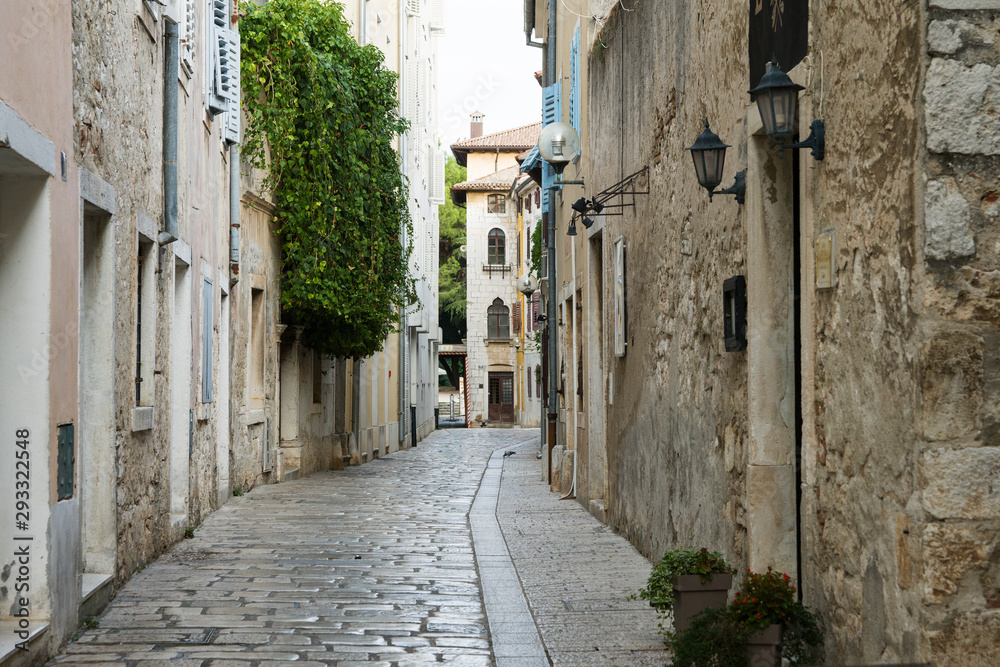 A deserted narrow street in an ancient city. The building is located opposite each other, between them is a narrow path lined with white stone. Porec, Croatia.