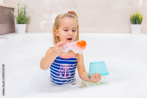 Fototapeta Little blonde girl taking bubble bath in beautiful bathroom